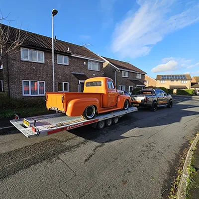 a tow truck towing a large orange truck down a street