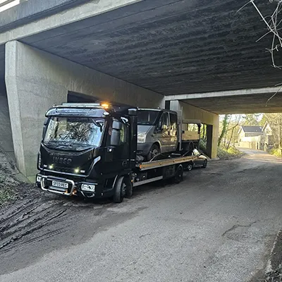 a tow truck towing a car under a bridge