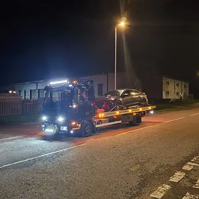 a tow truck towing a car down a street at night